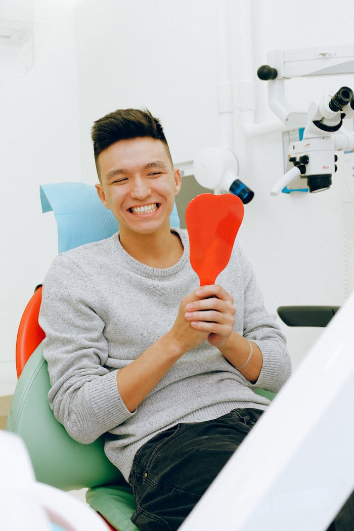 Smiling man holding a mirror during a dental checkup in a clinic setting.